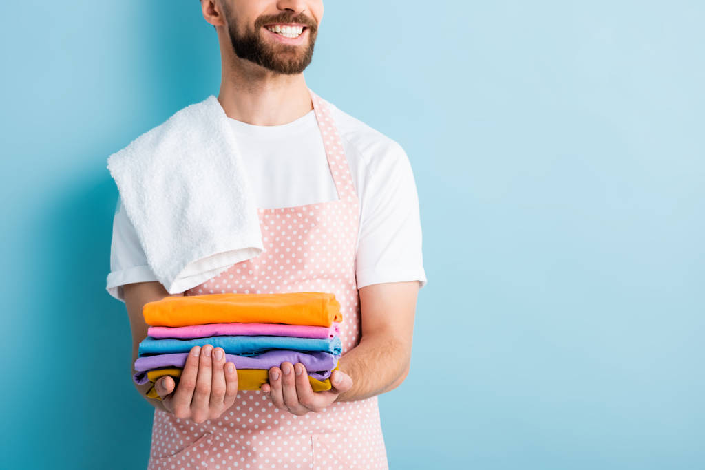 cropped view of cheerful bearded man holding clean clothing on blue - Photo, Image