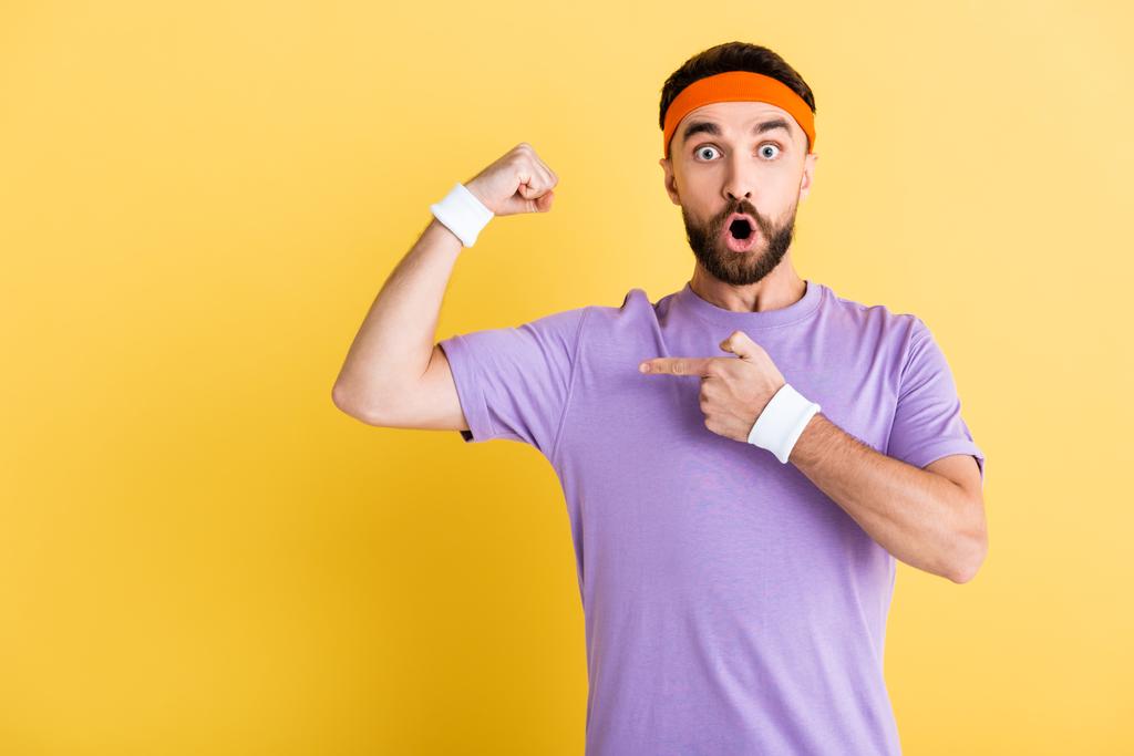 shocked man in headband pointing with finger and muscle isolated on yellow - Photo, Image