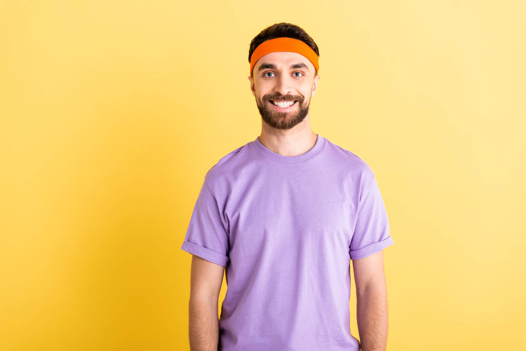 fröhlicher Sportler mit Stirnband lächelt vereinzelt auf gelb - Foto, Bild