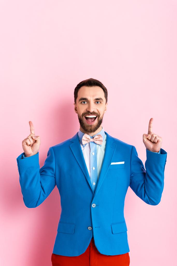 glücklicher bärtiger Geschäftsmann mit geöffnetem Mund, der mit den Fingern auf rosa zeigt  - Foto, Bild