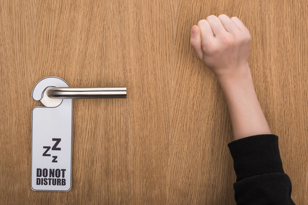 cropped view of woman knocking at door with do no disturb sign  - Photo, Image
