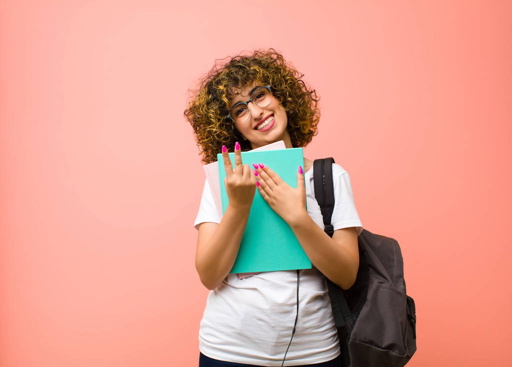 νεαρή όμορφη φοιτήτρια γυναίκα χαμογελά και αναζητούν φιλικό, δείχνει τον αριθμό επτά ή έβδομη με το χέρι προς τα εμπρός, μετρώντας αντίστροφα σε ροζ τοίχο - Φωτογραφία, εικόνα