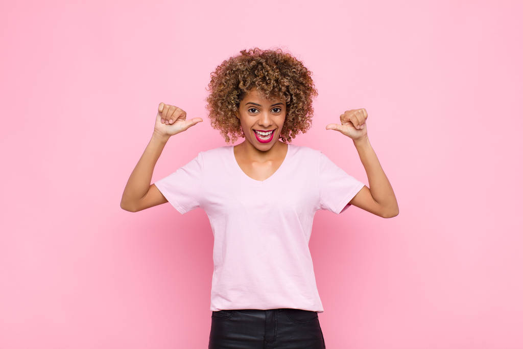 若いアフリカ系アメリカ人女性は誇り高く傲慢で自信に満ちて満足して成功しておりピンクの壁に対して自分自身を指しています - 写真・画像
