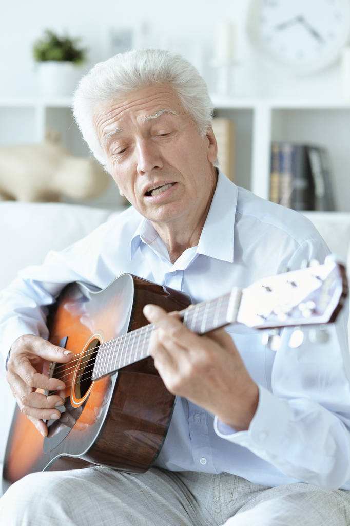 Gelukkig senior man met gitaar zittend op de Bank thuis - Foto, afbeelding