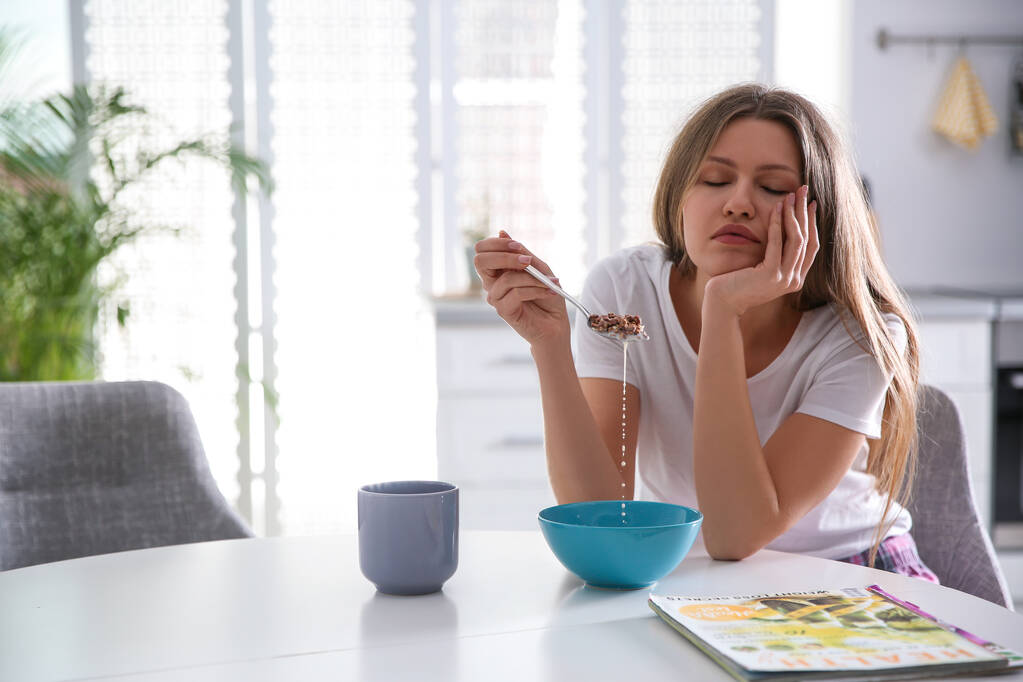 Сонная молодая женщина завтракает дома утром
 - Фото, изображение