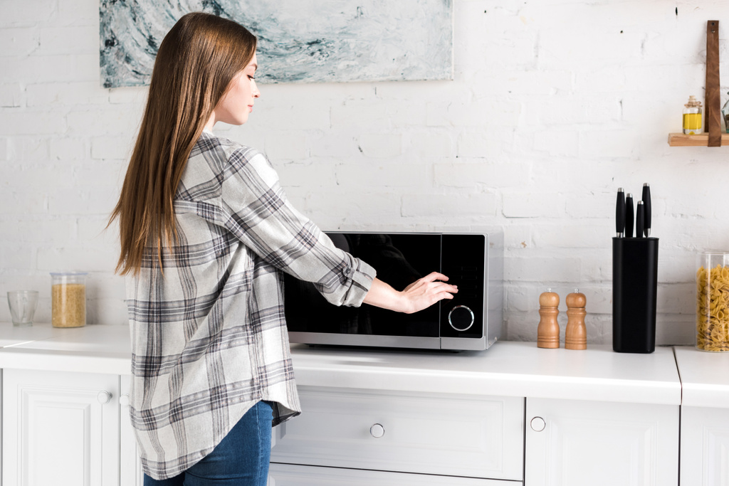 vista lateral de la atractiva mujer usando microondas en la cocina
  - Foto, Imagen