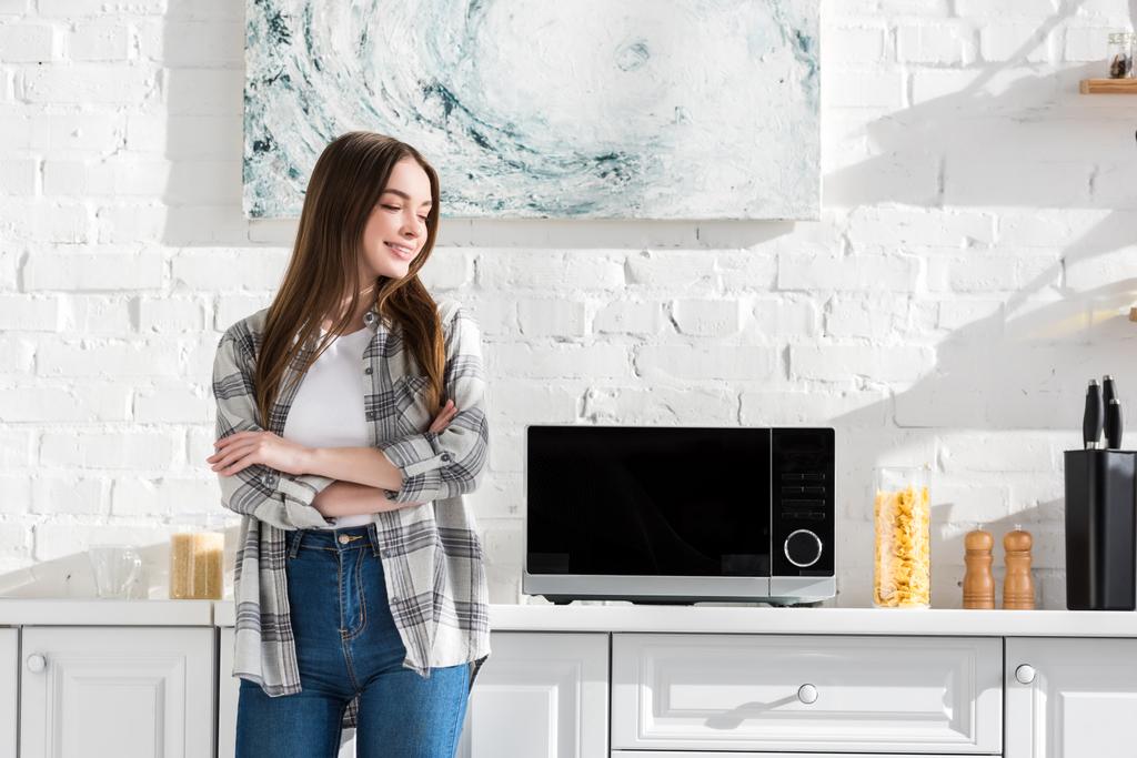 femme souriante et attrayante debout près de micro-ondes dans la cuisine
  - Photo, image