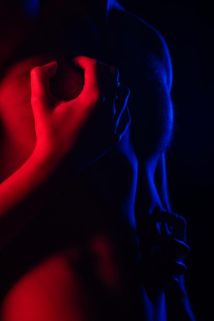 abgeschnittene Ansicht leidenschaftlicher Mann berührt sexy Freund nackten Oberkörper in rotem Licht isoliert auf schwarz - Foto, Bild