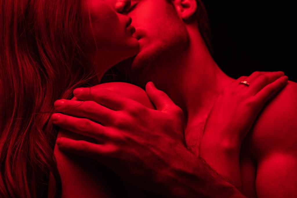 обрезанный вид страстной сексуальной молодой пары, целующейся в красном свете изолированы на черном
 - Фото, изображение