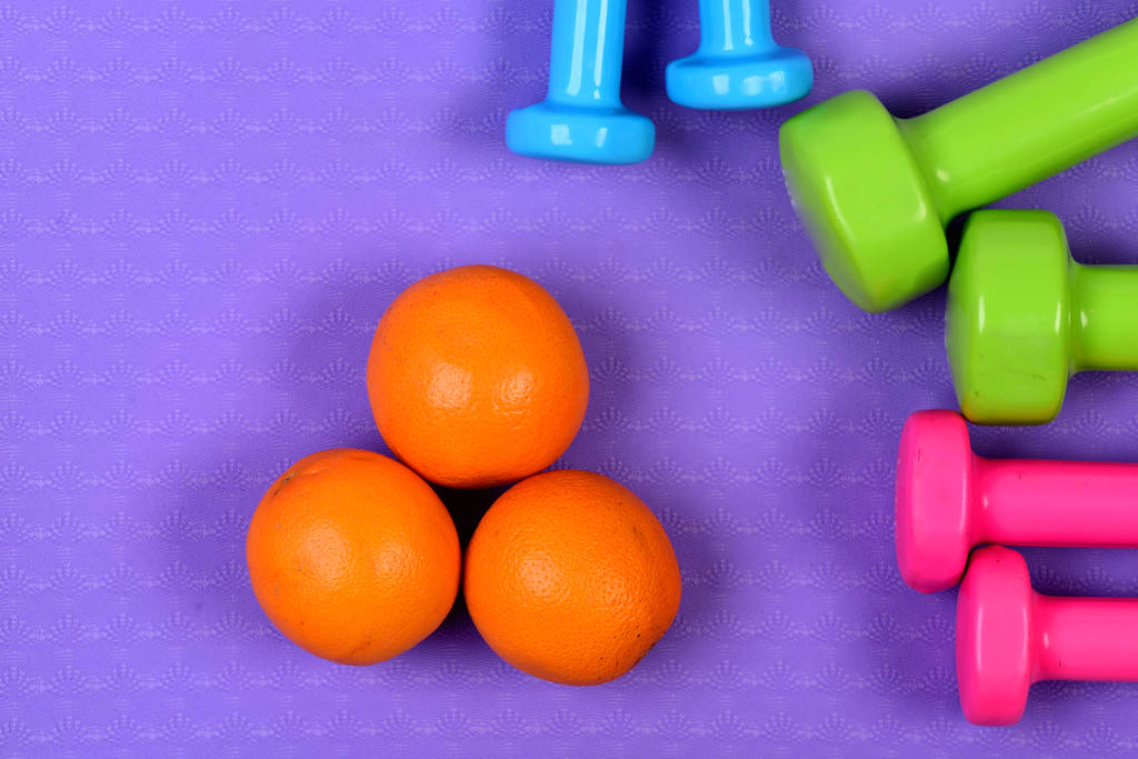 ダンベルと紫テクスチャ背景にオレンジ色の果物. - 写真・画像