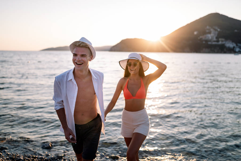 日没の夏休みにビーチでカップル。愛の中で美しい若者が歩く - 写真・画像