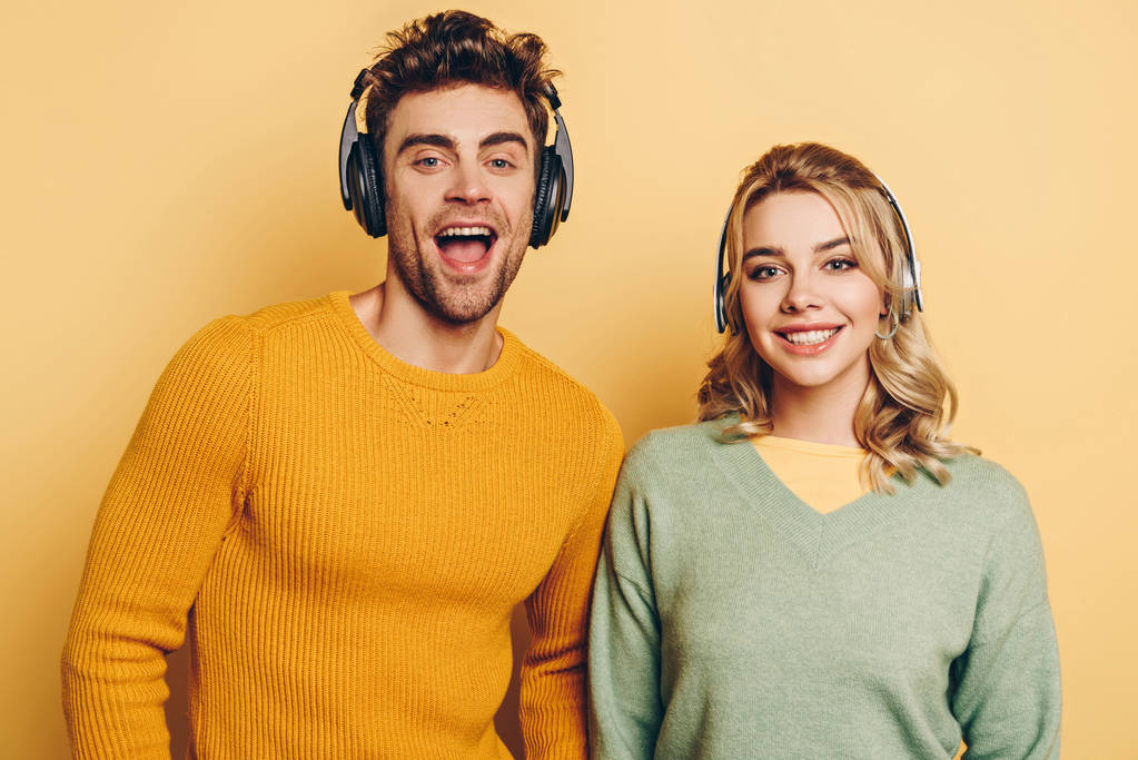 glückliche Männer und Frauen lächeln in die Kamera, während sie Musik in drahtlosen Kopfhörern auf gelbem Hintergrund hören - Foto, Bild