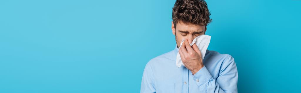 plano panorámico del hombre enfermo estornudando en servilleta de papel sobre fondo azul
 - Foto, imagen