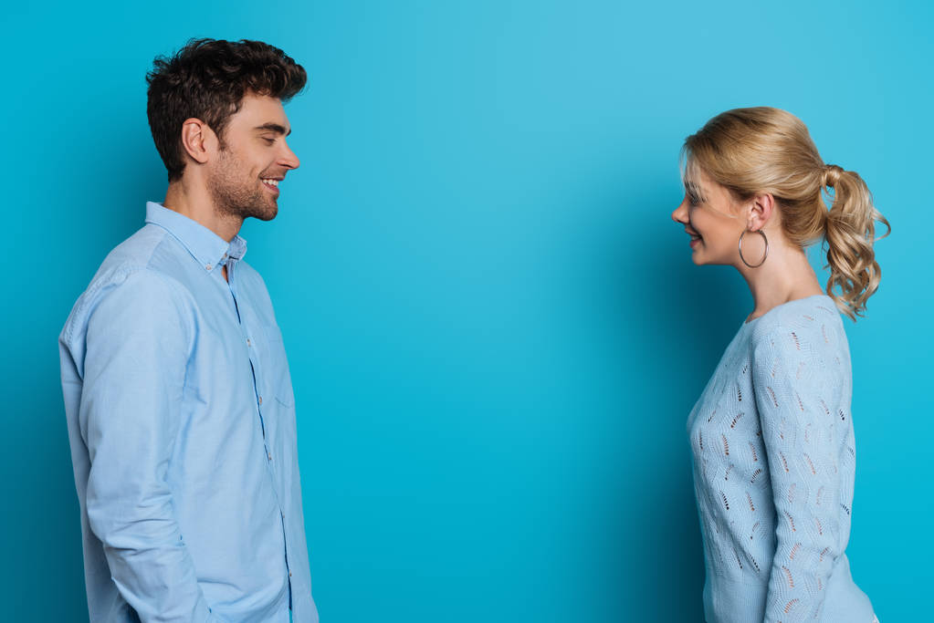 вид сбоку счастливых мужчины и женщины, улыбающихся друг другу на синем фоне
 - Фото, изображение