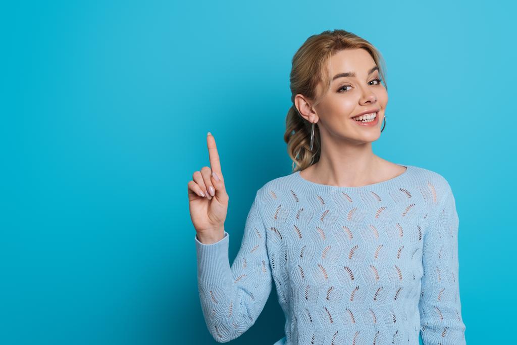 beautiful girl smiling at camera while showing idea sign on blue background - Photo, Image