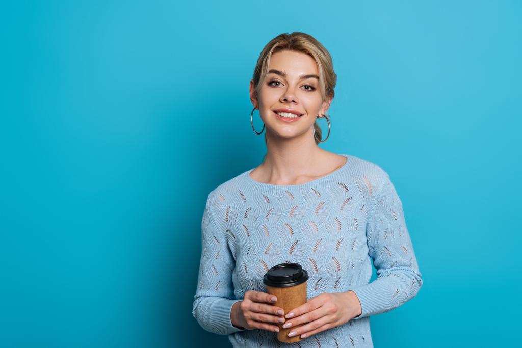 wesoła dziewczyna uśmiecha się do kamery trzymając kawę, aby przejść na niebieskim tle - Zdjęcie, obraz
