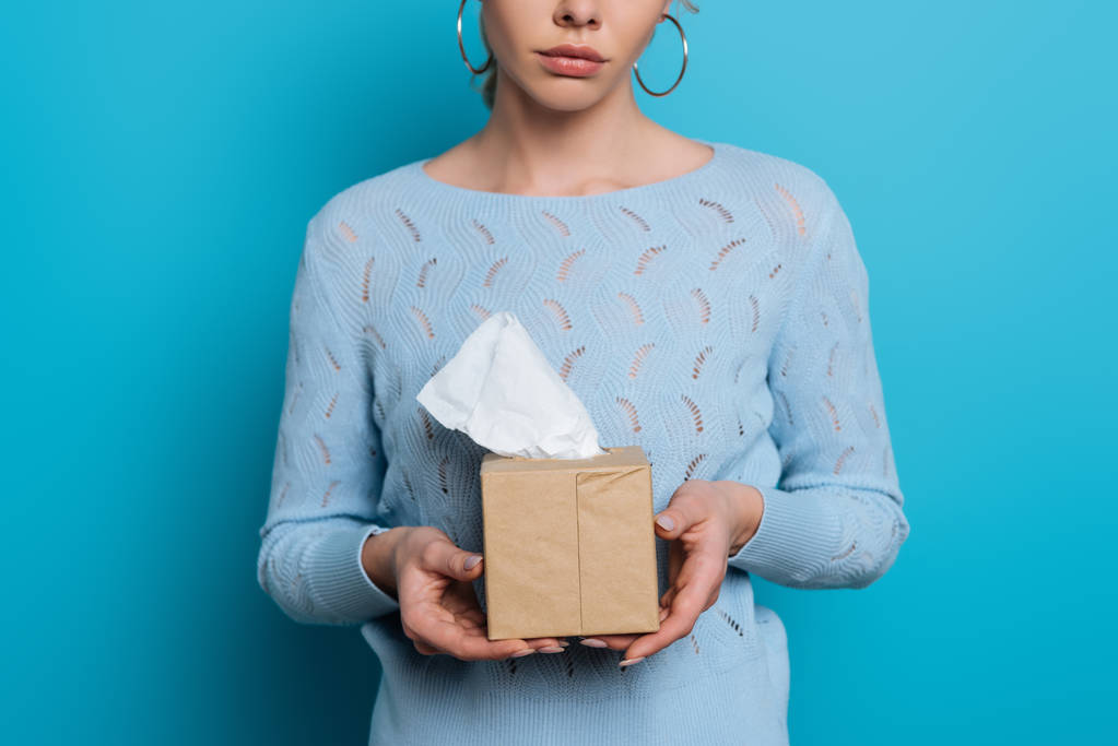 oříznutý pohled na rozrušený dívka drží balíček papírových ubrousků na modrém pozadí - Fotografie, Obrázek