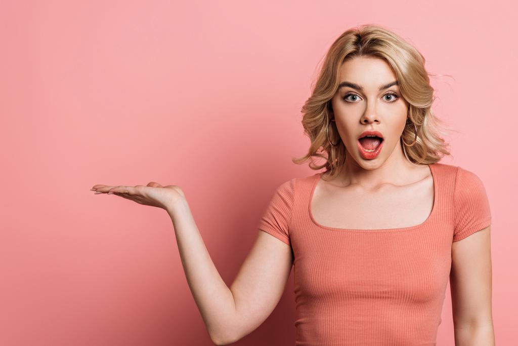 surprised girl pointing with hand while looking at camera on pink background - Photo, Image