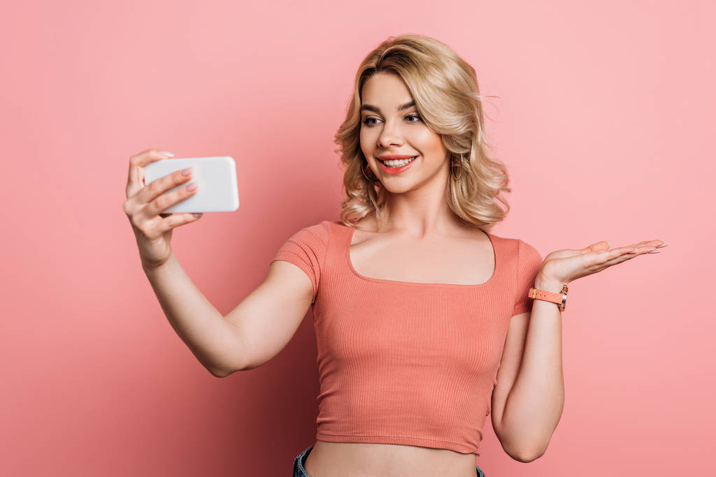 красива, усміхнена дівчина бере селфі на смартфон на рожевому фоні
 - Фото, зображення