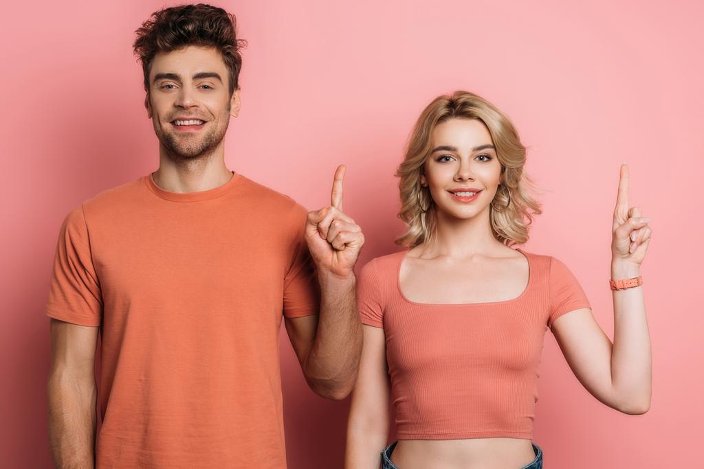 positive man and woman showing idea signs while looking at camera on pink background - Photo, Image