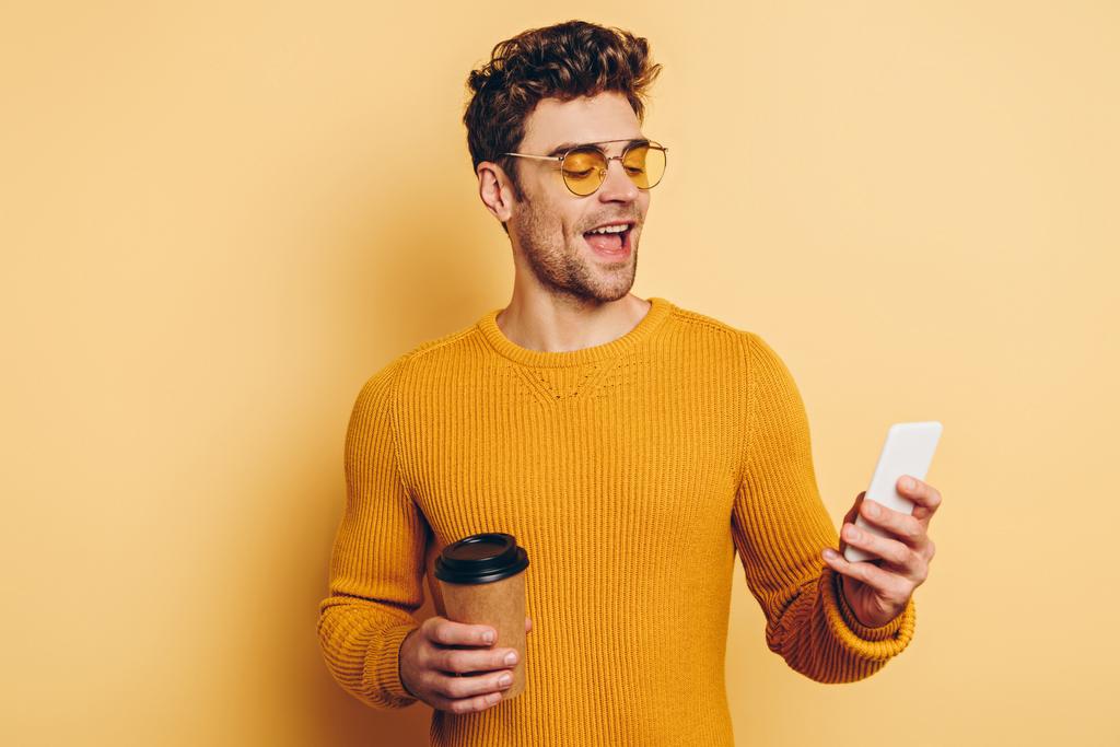 iloinen mies chattailuun älypuhelimeen pitäen kahvia mennä keltaisella pohjalla
 - Valokuva, kuva
