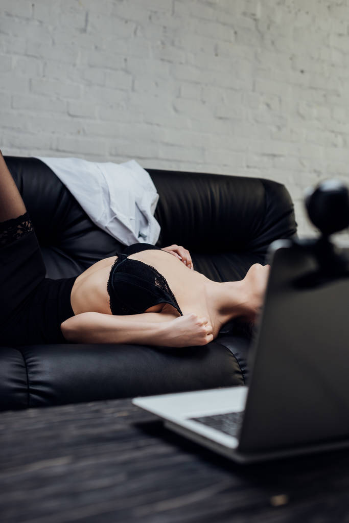 Cropped view of sexy girl in bra posing at laptop with web camera on couch - Photo, Image