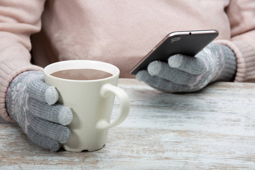 A man in warm clothes sits with a cup of hot drink in a street cafe. Rest during winter sports. A woman holds a phone in her hand. Close-up - 写真・画像