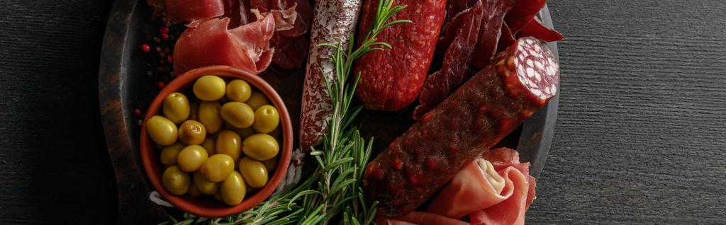 top view of delicious meat platter served with olives and herbs on wooden black table, panoramic shot - Photo, Image
