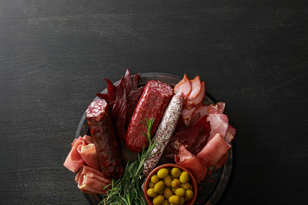 vista superior de la deliciosa bandeja de carne servida con aceitunas y hierbas sobre una mesa negra de madera
 - Foto, imagen
