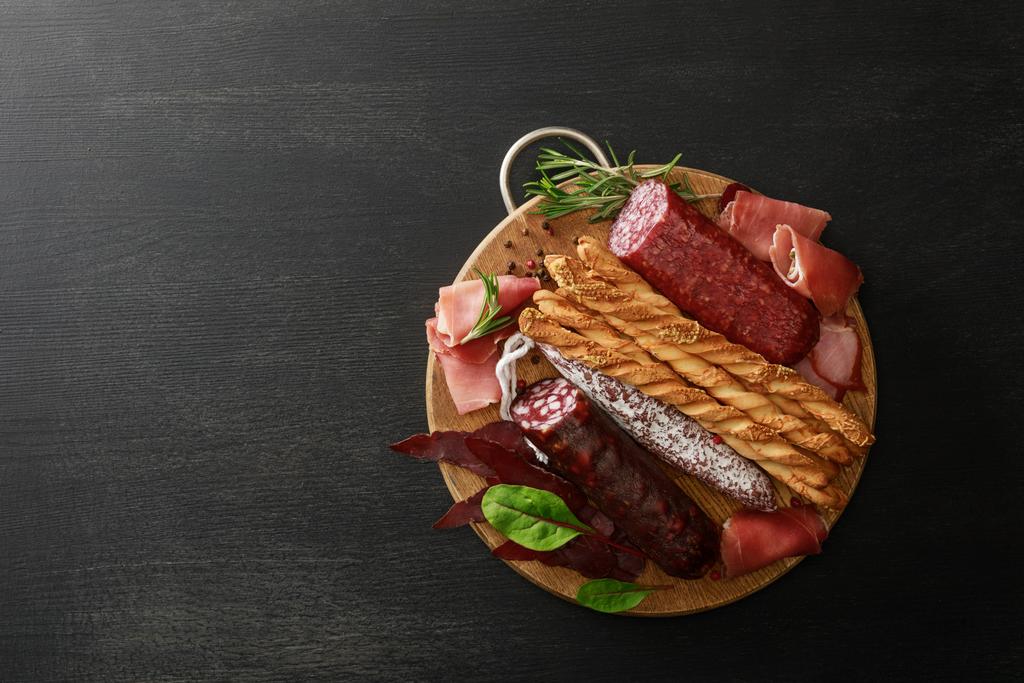 vista superior de la deliciosa bandeja de carne servida con palitos de pan y hierbas a bordo sobre una mesa negra de madera
 - Foto, imagen