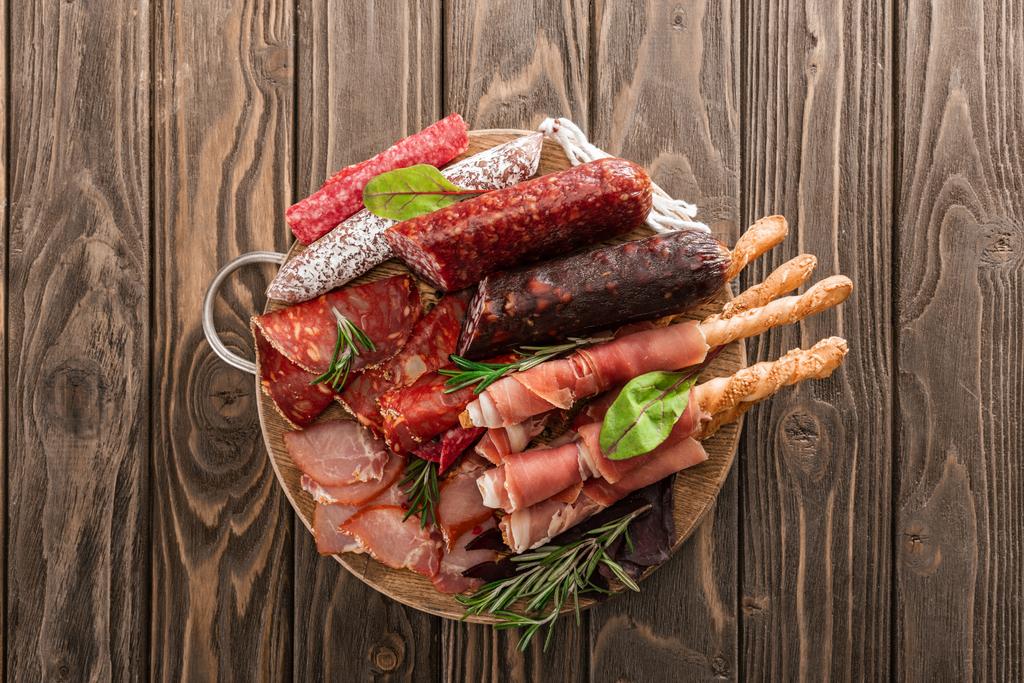 top view of delicious meat platter served with rosemary and breadsticks on wooden board - Photo, Image