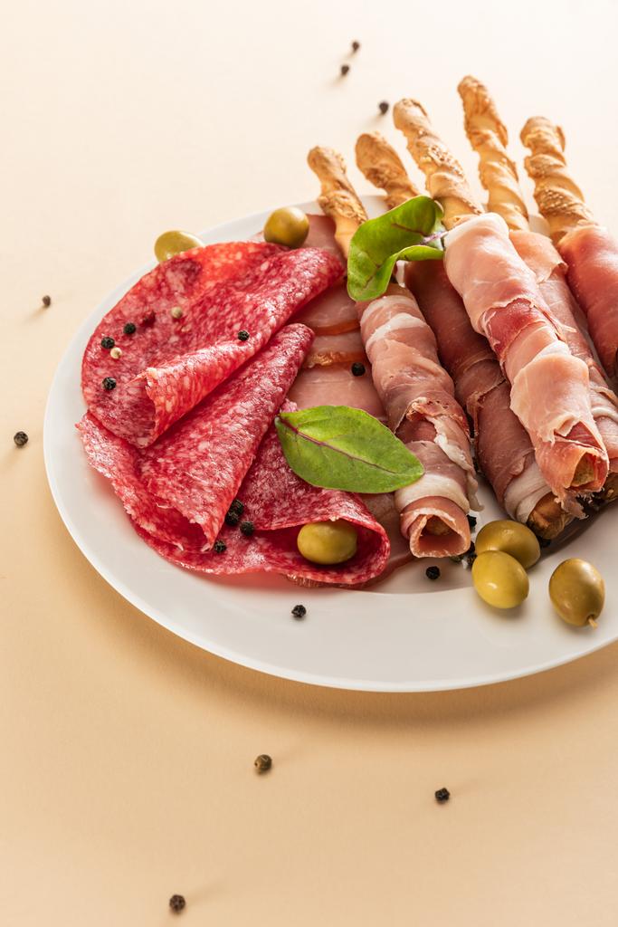 вкусное мясное блюдо подается с оливками и хлебными палочками на тарелке на бежевом фоне
 - Фото, изображение