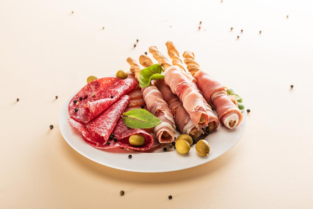 köstliche Fleischplatte serviert mit Oliven und Semmelstangen auf Teller auf beigem Hintergrund - Foto, Bild