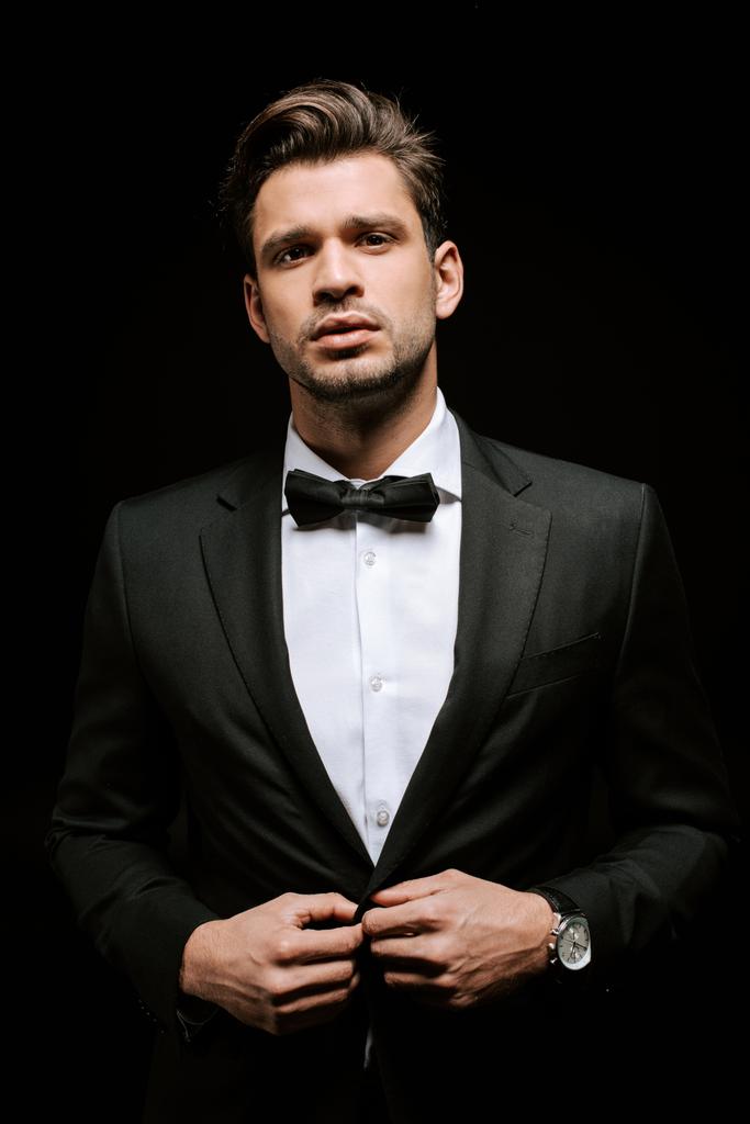 Eleganter Mann im Anzug berührt Blazer isoliert auf Schwarz  - Foto, Bild