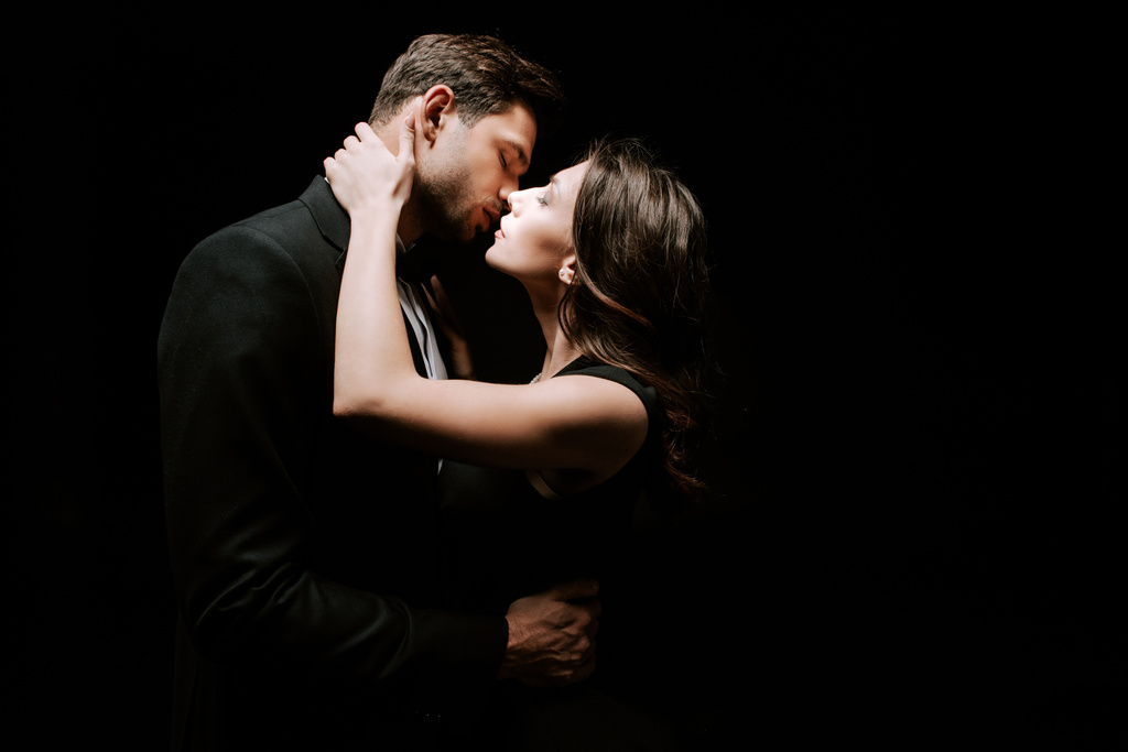 Seitenansicht der attraktiven Frau küsst mit Mann isoliert auf schwarz  - Foto, Bild