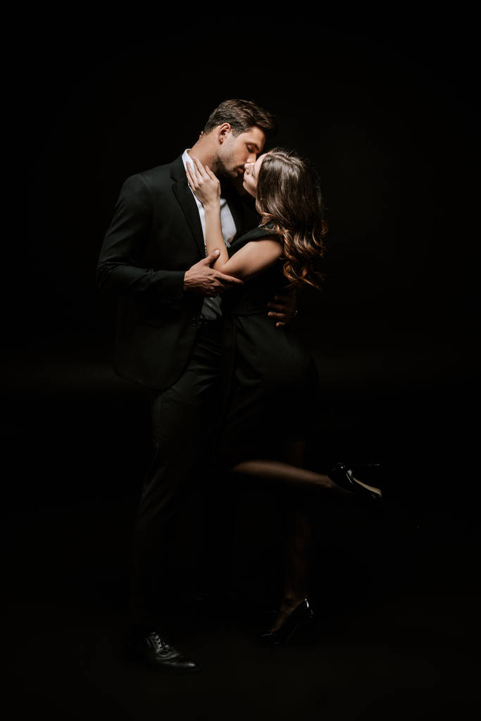 γυναίκα φιλάει όμορφο άνδρα με κοστούμι απομονωμένο σε μαύρο  - Φωτογραφία, εικόνα