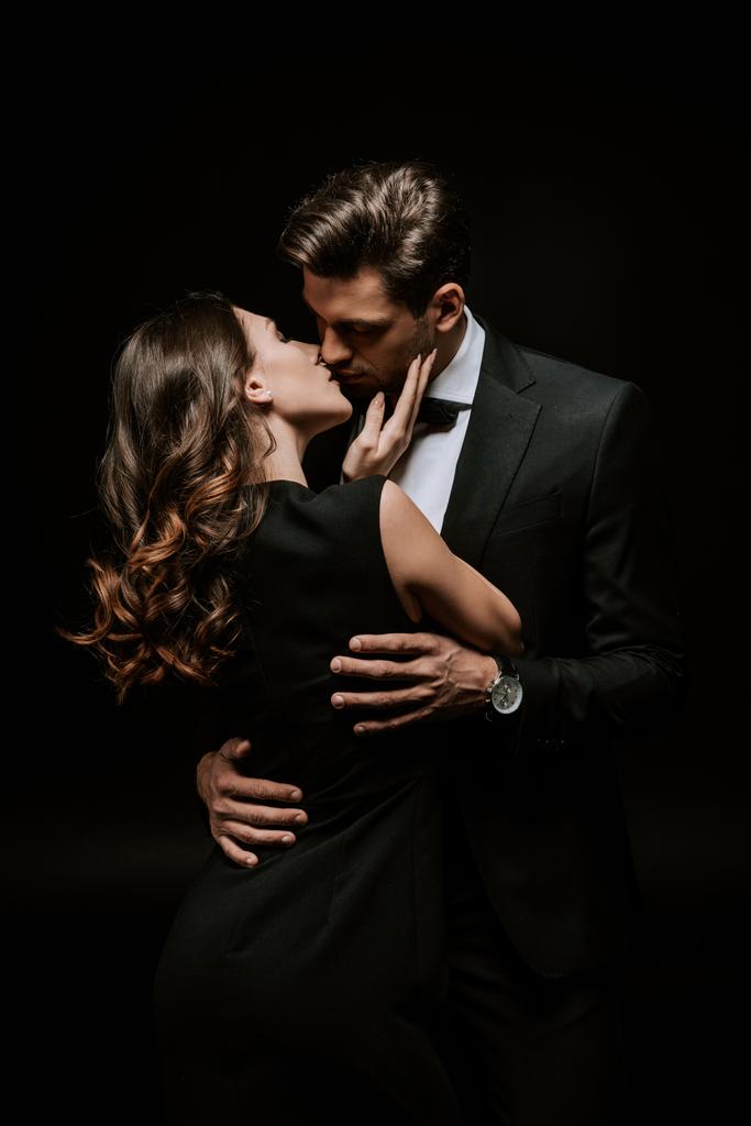 beautiful woman kissing handsome man in suit isolated on black  - Photo, Image