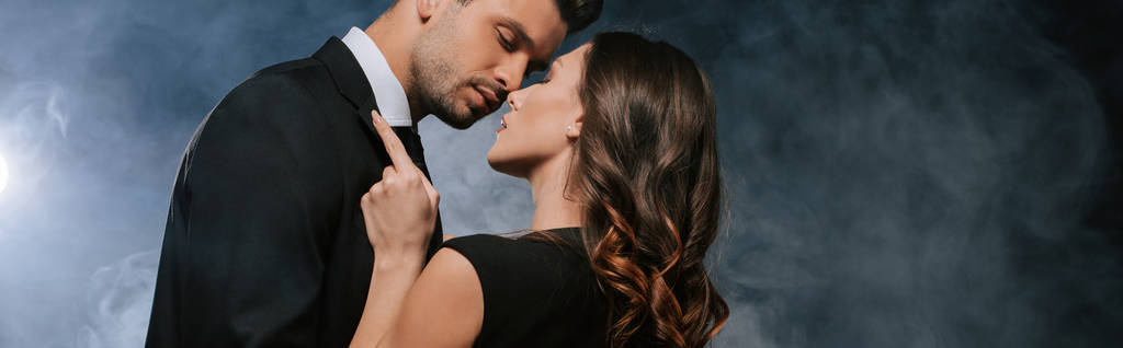 tiro panorâmico de mulher abraçando homem bonito em preto com fumaça
  - Foto, Imagem