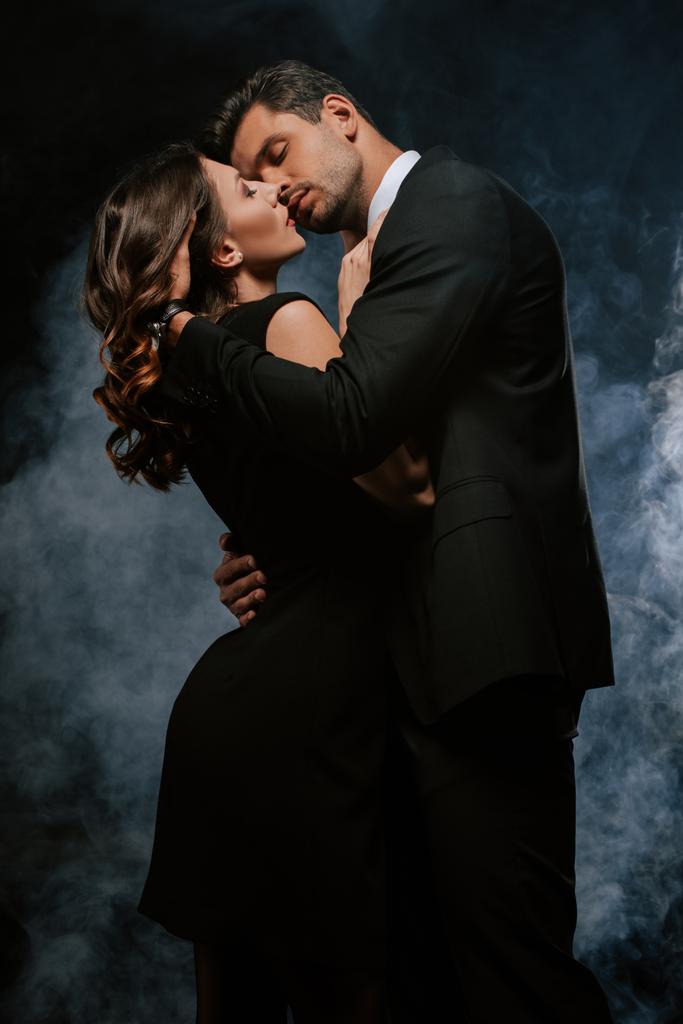 handsome man in suit hugging sensual woman on black with smoke  - Photo, Image