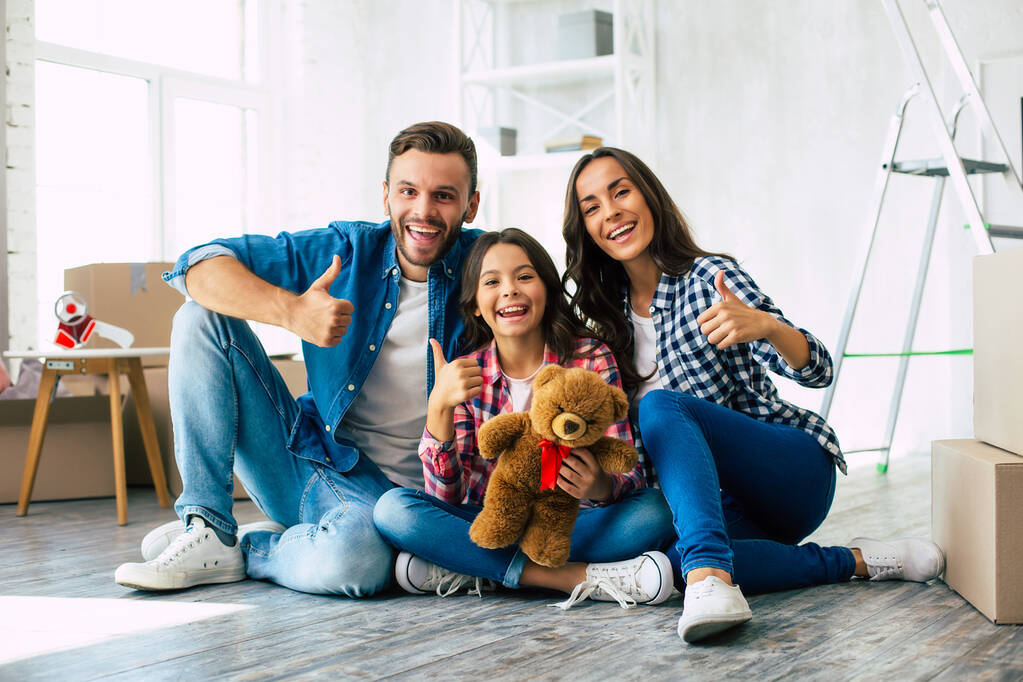 Looking forward to our bright future. Young father in denim outfit little teenage daughter and beautiful mother are sitting on the floor, hugging and smiling happily after moving house. - Photo, Image