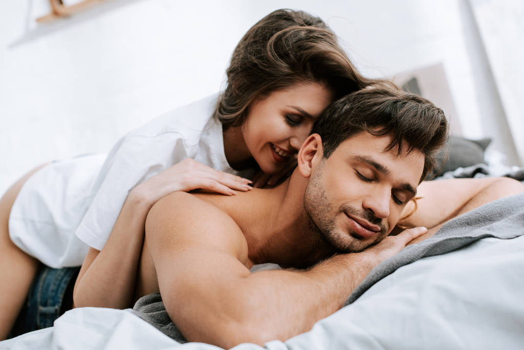 fröhliche Frau liegt mit muskulösem Freund im Bett  - Foto, Bild