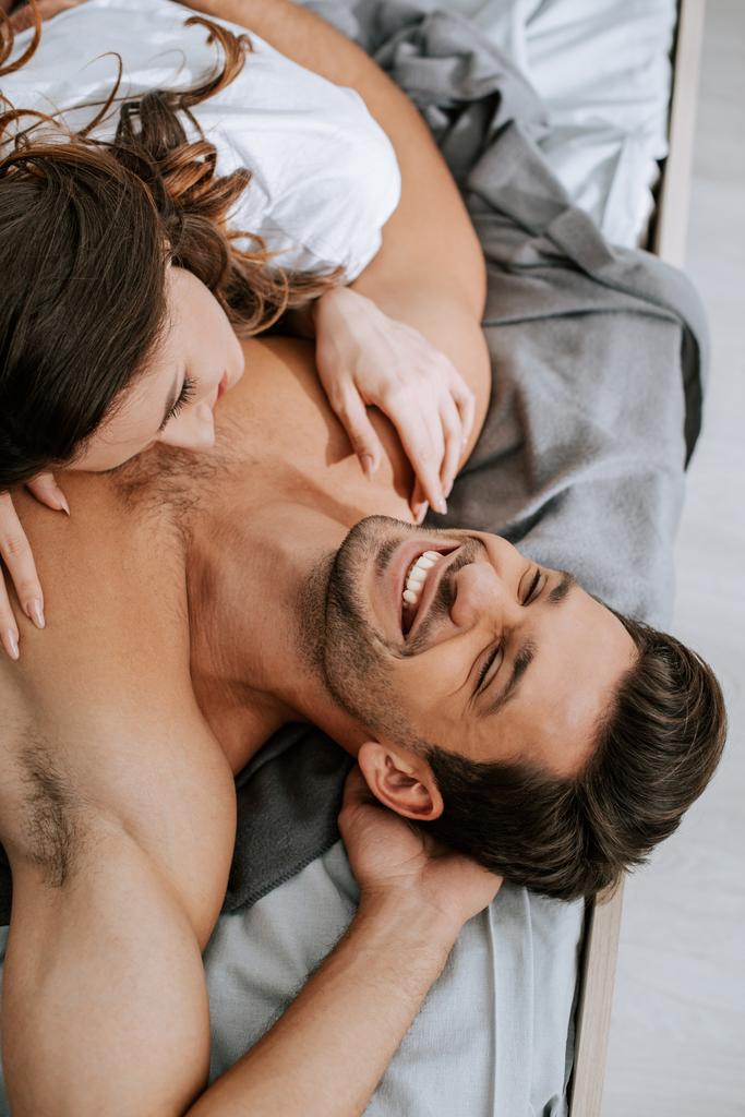 vista dall'alto di felice giovane donna sdraiata sul letto con fidanzato muscoloso
  - Foto, immagini