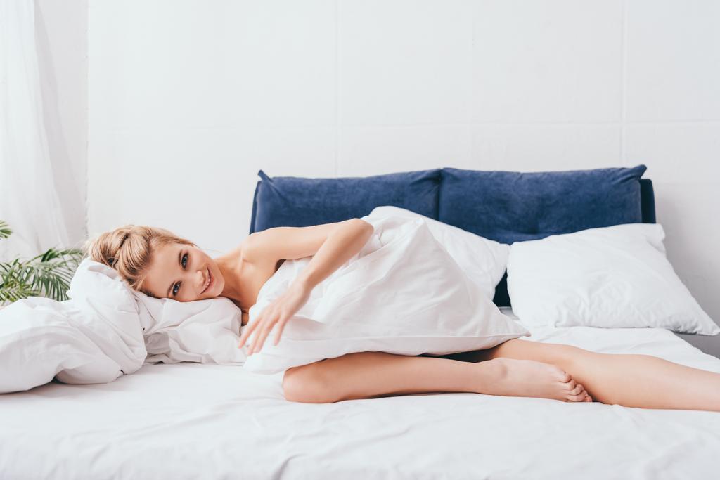 donna sorridente sdraiata in lenzuola sul letto al mattino
 - Foto, immagini