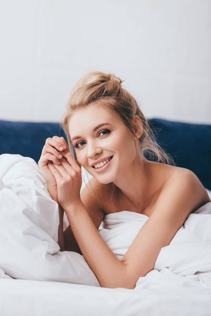 χαρούμενη νεαρή γυναίκα ξαπλωμένη σε σεντόνια στο κρεβάτι το πρωί - Φωτογραφία, εικόνα