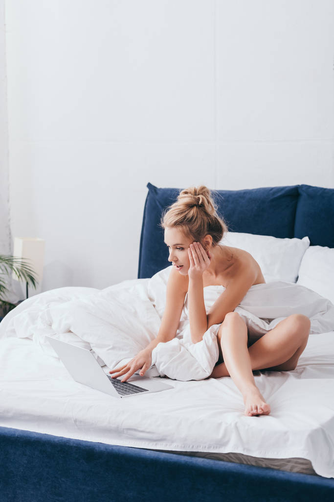 šokované žena pomocí notebooku na posteli s prostěradly v dopoledních hodinách  - Fotografie, Obrázek
