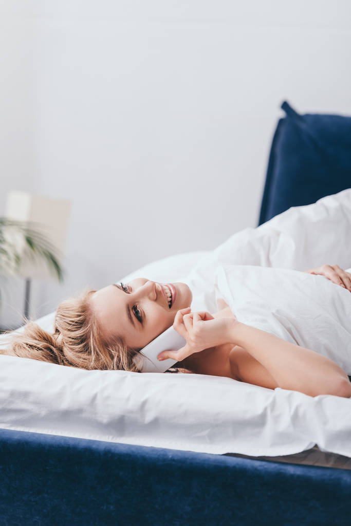 piękna szczęśliwa kobieta rozmawia rano na smartfonie w łóżku  - Zdjęcie, obraz