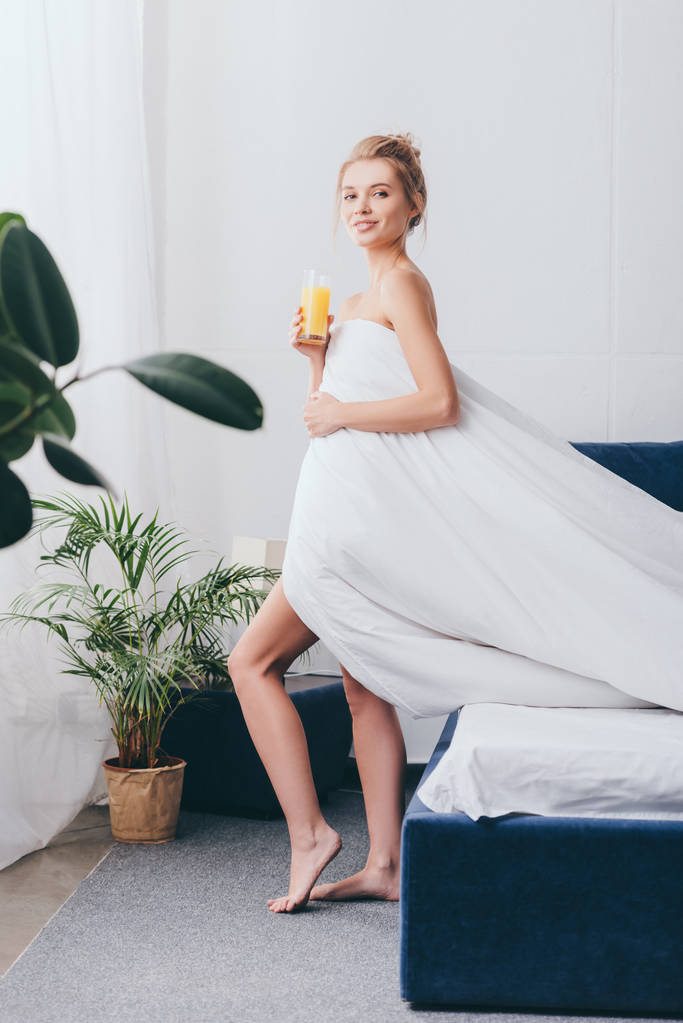 hermosa joven con vaso de jugo en sábanas blancas en el dormitorio por la mañana
 - Foto, imagen