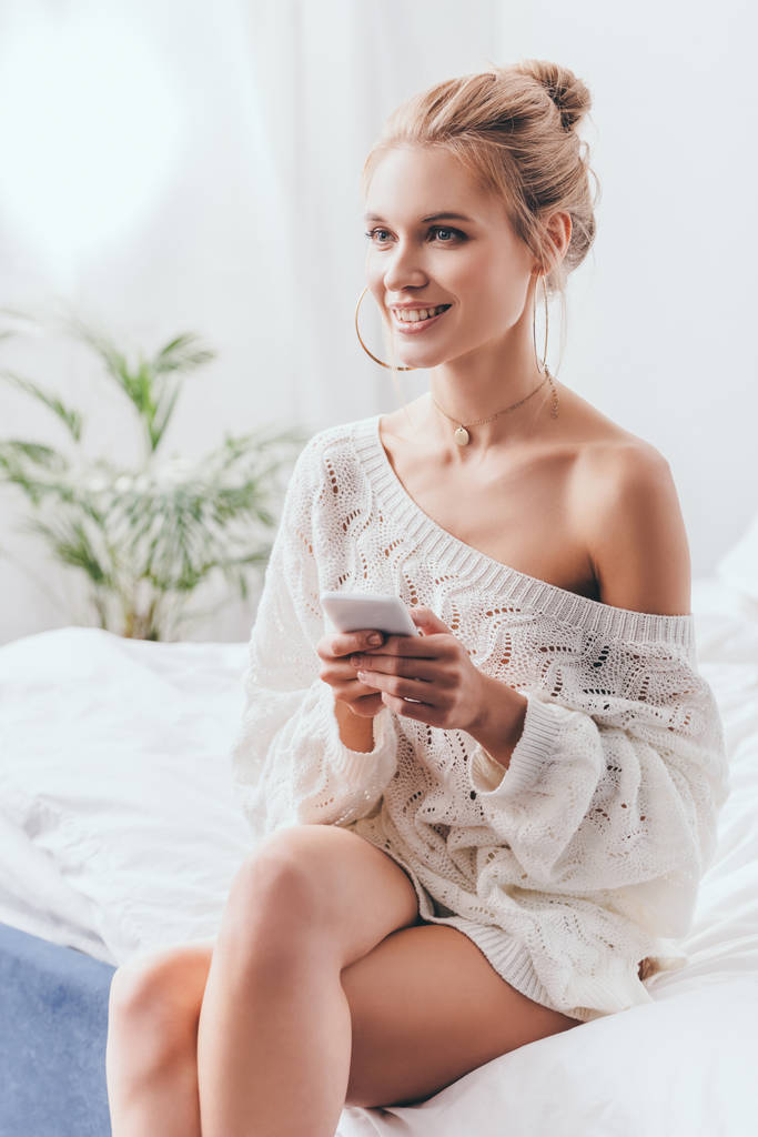 krásná usmívající se žena pomocí smartphone na posteli v dopoledních hodinách  - Fotografie, Obrázek