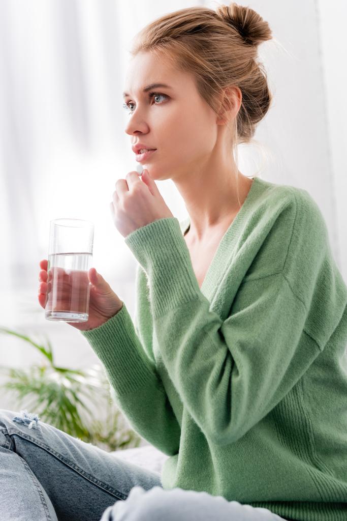 hermosa mujer tomando pastillas y sosteniendo vaso de agua en el dormitorio
 - Foto, imagen