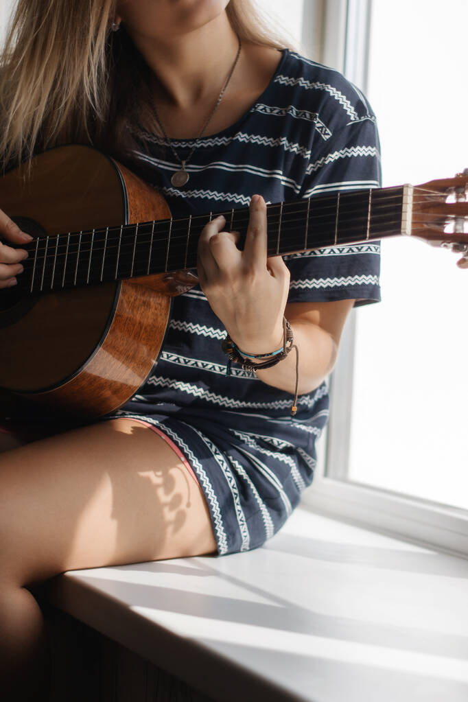Schnappschuss einer Frau in gestreiftem Kleid, die auf Fensterbank Gitarre spielt - Foto, Bild